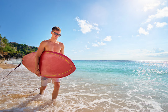 Hobby and vacation. Holiday on the beach. Young man carrying surf board.