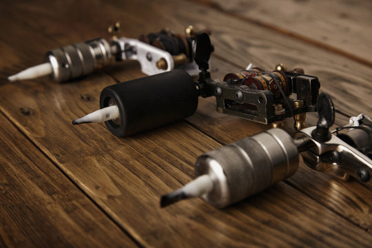Three different custom professional tattoo guns arranged on a brown wooden table side view, focused on center machine