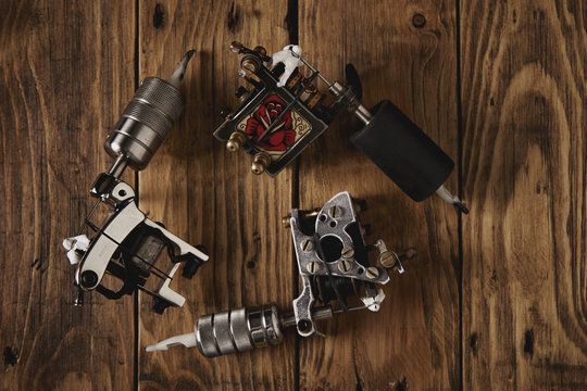 Three custom made professional induction tattoo machines arranged in round on a brown wooden table, top view