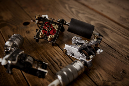 Close up on three custom made professional induction tattoo machines arranged in round on a brown wooden table