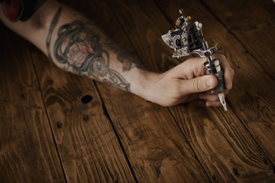 Close up of a man's hand holds new custom made steampunk style tattoo gun above brushed vintage wooden table