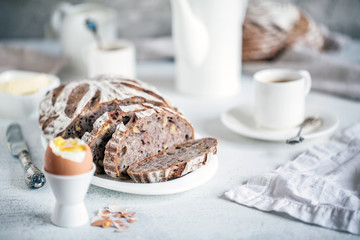 Artisan sourdough bread with rye flakes and walnuts in light breakfast composition with white porcelain, coffee, butter and hard-boiled egg
