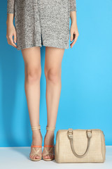 Women's sexy legs in sandals high-heeled shoes with beige bag on a blue background.