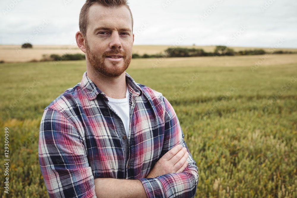 Poster portrait of farmer standing with arms crossed in the field