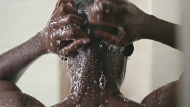 Rear view of black man washing head with shampoo under shower