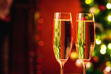 Beautiful two glasses of champagne standing on the table in the background of a blurred room with a decorated Christmas tree and fireplace. Soft focus. Shallow DOF