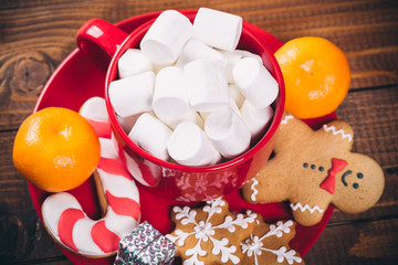 Beautiful Christmas background with Cup of marshmallows and a platter of gingerbread, tangerines, candy  and gifts on wooden board table