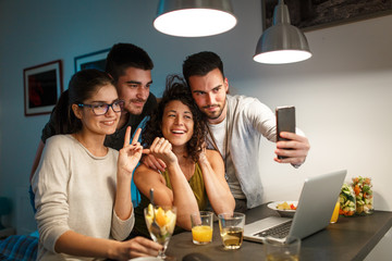 Friends sitting together in living room and watching movie on on laptop and taking selfie