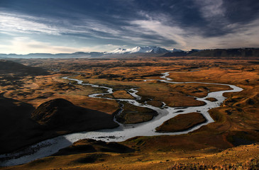 Snowcapped high ice snow mountain peaks with glaciers above orange steppe with white water river...