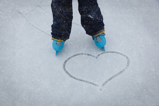 love skating concept - child feet in skates and heart on snow