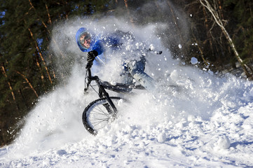 Extreme cyclist riding mountain bike in flying snow near winter forest in sunny cold day 