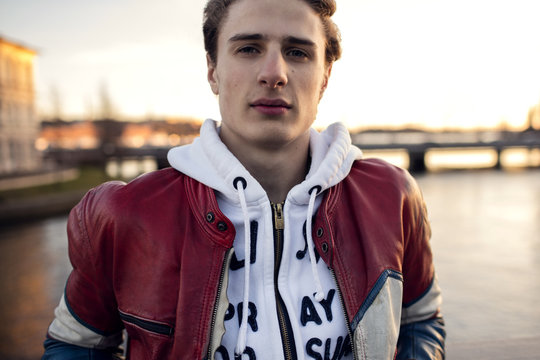 Portrait of teenager wearing jacket standing against canal in city