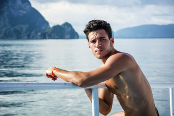 Portrait of young handsome bare-chested brunet man looking away against seascape on a boat or...
