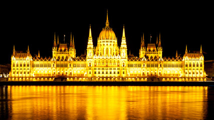Fototapeta premium Night panoramic view of illuminated historical building of Hungarian Parliament, aka Orszaghaz, reflected in the water with typical symmetrical architecture and central dome on Danube River embankment