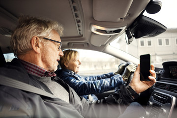 Man holding smart phone while sitting by senior woman driving car in city