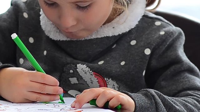 Cute happy little girl playing with crayons. Christmas background. Christmas lights background
