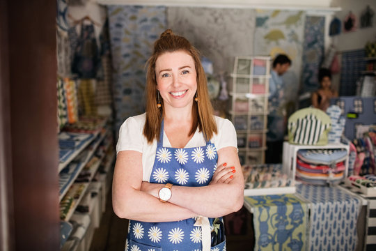 Portrait of smiling owner standing with arms crossed while colleagues working in shop