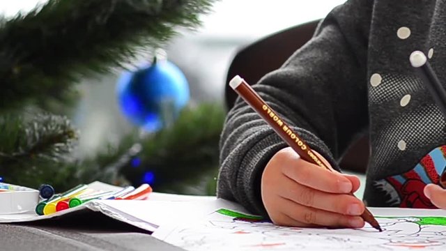 Cute happy little girl playing with crayons. Christmas background. Christmas lights background