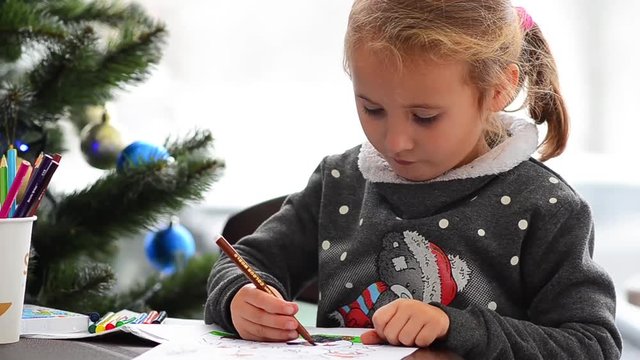 Cute happy little girl playing with crayons. Christmas background. Christmas lights background