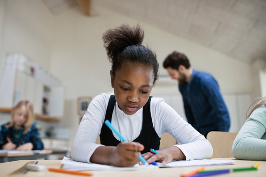 Young student concentrates and writes at desk in classroom