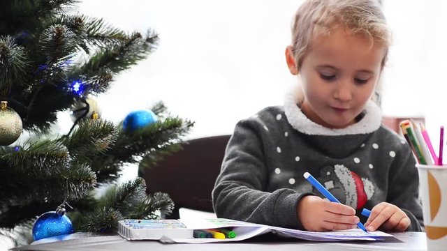 Cute happy little girl playing with crayons. Christmas background. Christmas lights background
