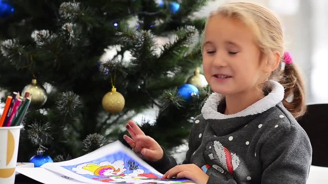 Cute happy little girl playing with crayons. Christmas background. Christmas lights background