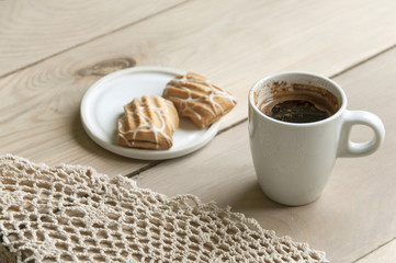 Cozy home still life. A cup of coffee and plate with cookies on knitted napkin on light wooden background. Close up.