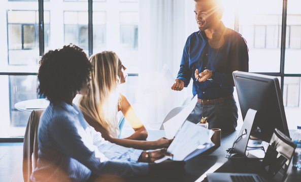 Young team of coworkers making great meeting discussion in modern coworking office.Hispanic businessman talking with two beautiful womans.Teamwork process.Horizontal,blurred background,flares effect.
