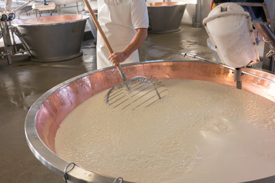 Worker stirring curd in copper tub of cheese factory making parmesan 