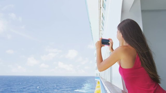 Cruise ship vacation woman taking photo with smart phone camera enjoying travel at sea. Girl using smartphone to take picture of ocean. Woman in dress on luxury cruise liner boat.