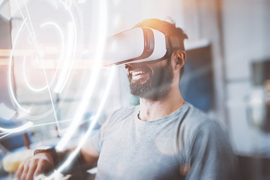 Concept of digital screen,connection and interfaces.Smiling hipster enjoyingvirtual reality glasses in modern design home studio.Smartphone use with VR goggles headset.Horizontal,flare,blurred.
