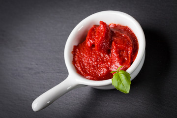 Fresh tomato sauce in small white bowl decorated leaf of basil. The most famous of food ingredients in italian kitchen.