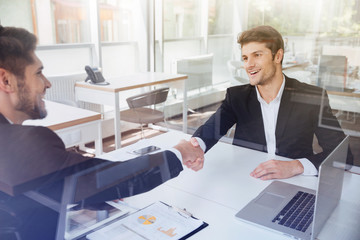 Two cheerful successful young businessmen shaking hands on busin
