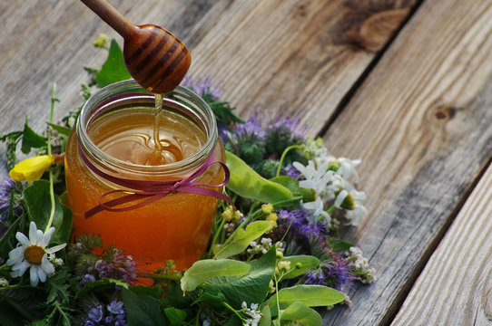 Honey in a glass jar with flowers melliferous herbs on a wooden surface. Honey with flowers.