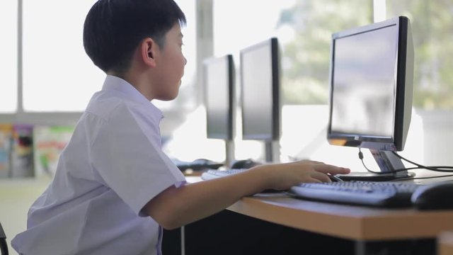 Happy Asian child using a desktop computer at school .
