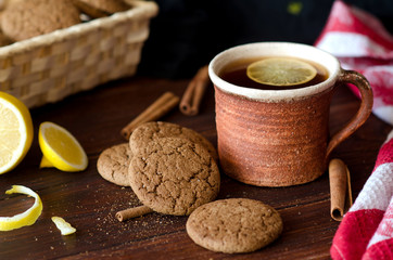 Печенье, чашка чая, лимон и корица на деревянном столе