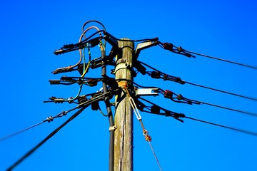 Old electricity pole with wires against blue sky.