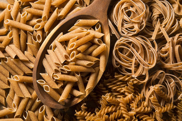 Wholemeal penne into a spoon. Integral Pasta over a wooden table