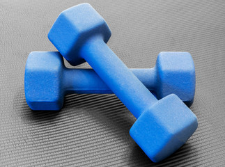 Two blue dumbell weights on an open black exercise yoga mat