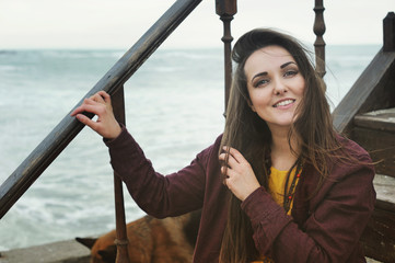 Beautiful smiling brunette woman sitting on a stairs against seascape, smiling and looking at camera