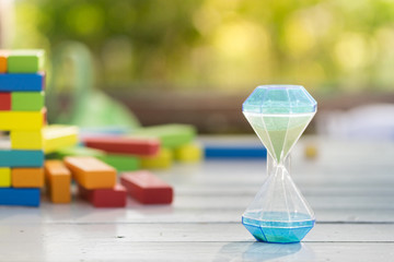 Hourglass on the wooden table with colorful wooden block as a ba