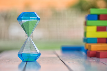 Hourglass on the wooden table with colorful wooden block as a ba