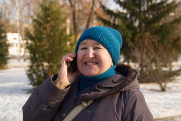 Portrait of mature woman talking on phone outdoor. Senior lady smiling and   the  in park at winter sunny day