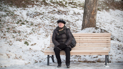 Fototapeta premium Portrait of the old woman on the bench at winter day in park
