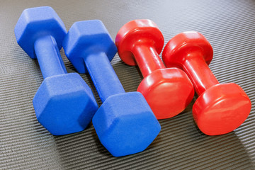 Two sets of different sized dumbbells, red and blue, on a black