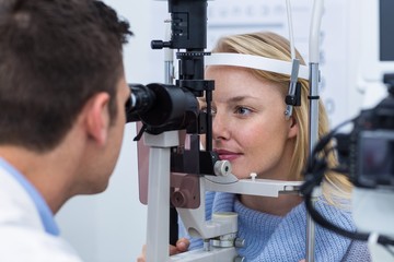 Optometrist examining female patient on slit lamp - obrazy, fototapety, plakaty
