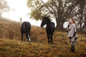 Woman with her horses. Concept about people and animals. Early morning. Misty mountain. Woman in boho style.