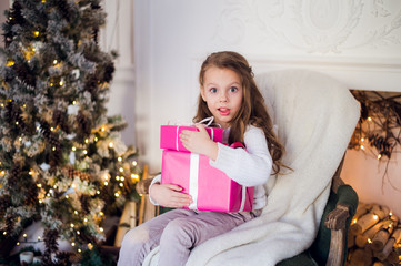 picture of beautiful girl with gift boxes sitting on armchair at home. Decorated christmas tree background