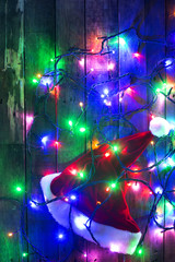 Fototapeta na wymiar Santa Claus hat on wood background surround by light bulbs
