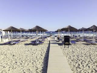View on Mediterranean Sea sunny sand beach with rows of bedstones under straw umbrellas.  Nei Pori village, Pieria, Greece.